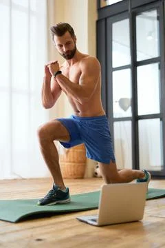Handsome young man using laptop and doing lunges at home Stock Photos
