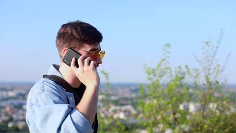 Handsome young man using mobile phone for call outside on sunny background. Trav 動画素材 132548602