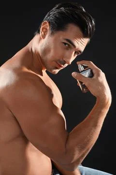 Handsome young man using perfume on black background Fotos Stock