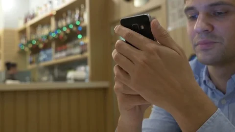 Handsome young man using a smartphone, drinking coffee and smiling while Video stock 83233664
