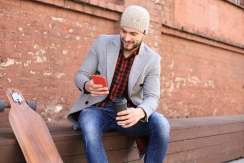 Handsome young man using smartphone, resting, sitting with longboard. Stock Photos