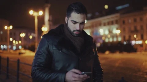 Handsome young man walking down the night snowy street and using his smartphone Video stock 84652577