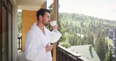 Handsome young man in white bathrobe standing on balcony of hotel room, enjoying Video stock 156969699