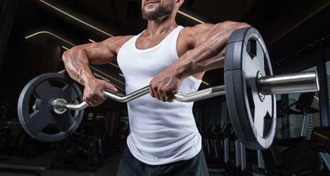 Handsome young man working out with a barbell in the gym. Shoulder pumping... Stock Photos
