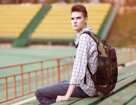 Handsome young pensive man with backpack, modern hipster sitting on a bench Stock Photos
