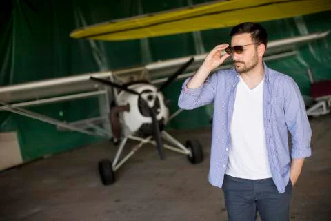 Handsome young pilot checking airplane in the hangar and using mobile phone Stock Photos