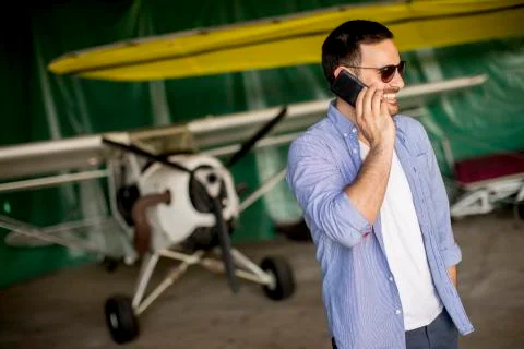 Handsome young pilot checking airplane in the hangar and using mobile phone Foto stock