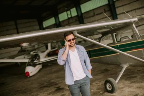 Handsome young pilot checking airplane in the hangar and using mobile phone Stock Photos