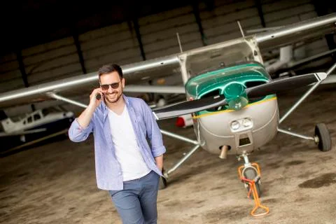 Handsome young pilot checking airplane in the hangar and using mobile phone Stock Photos