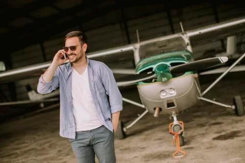 Handsome young pilot checking airplane in the hangar and using mobile phone Stock Photos
