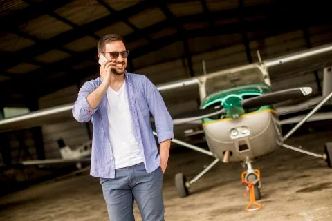 Handsome young pilot checking airplane in the hangar and using mobile phone 写真素材