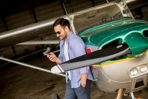 Handsome young pilot checking airplane in the hangar and using mobile phone Foto stock