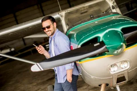 Handsome young pilot checking airplane in the hangar and using mobile phone 스톡 사진