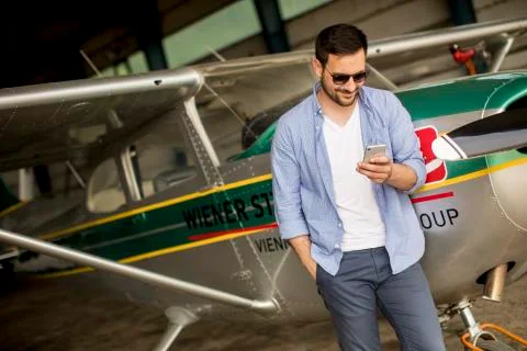 Handsome young pilot checking airplane in the hangar and using mobile phone Foto stock