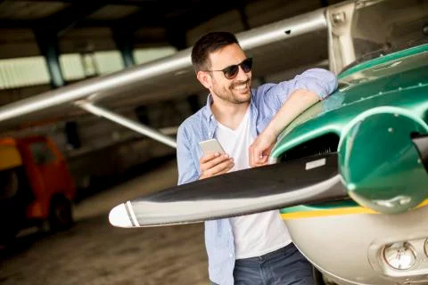 Handsome young pilot checking airplane in the hangar and using mobile phone 写真素材