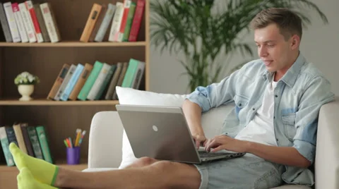 Handsome young student sitting on sofa and using laptop Video stock 27692066