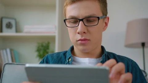 Handsome young student using tablet computer device while sitting on the couch Stock Footage 75971806