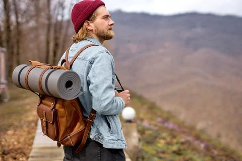 Handsome young stylish man in denim jacket with backpack, walks in nature. Stock Photos