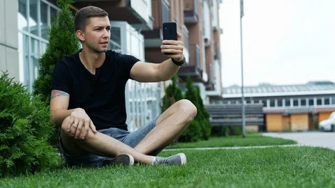 Handsome young stylish man making selfie sitting on the grass Stock Footage 111974812