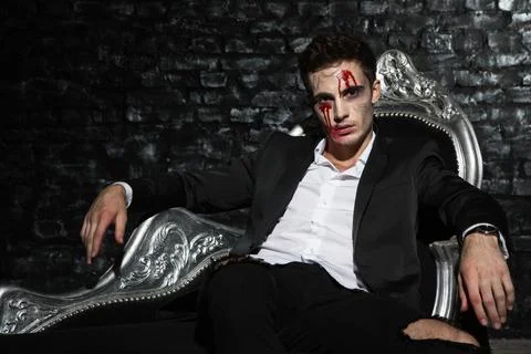 Handsome young vampire resting on silver couch Stock Photos