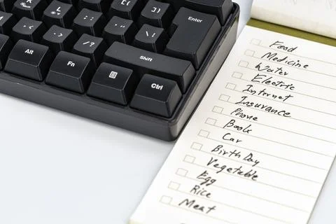Handwritten checklist notepad beside black mechanical keyboard with monthly Stock-Fotos