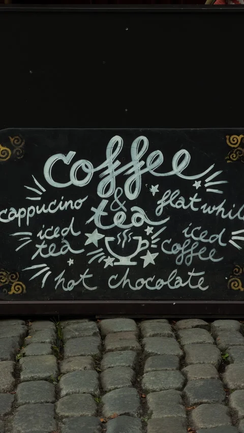 Handwritten coffee tea and hot chocolate chalkboard sign beside cobblestone Stock Footage 337734894