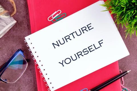 A handwritten note stating NURTURE YOURSELF is placed on a bright red noteboo Stock Photos