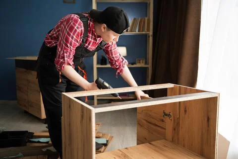 Handyman in blue coverall using drill for furniture assembly, she working in  Stock Photos