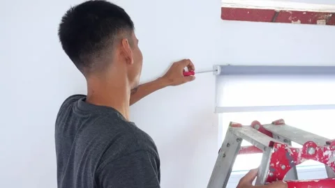 Handyman expertly installing modern roller blinds with precision using Stock Footage 323805512