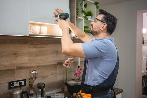 Handyman installing kitchen cabinets using a cordless screwdriver Stock Photos