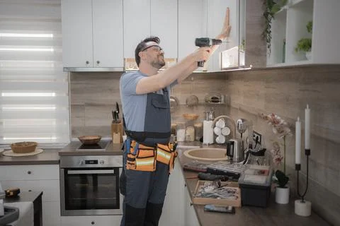 Handyman installing kitchen cabinets using a cordless screwdriver Stock Photos