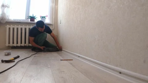 Handyman installing plastic baseboard molding in a room Stock Footage 326150652