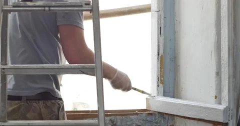 Handyman paints a window frame with white paint with a paint brush. Hand in Stock Footage 152836100