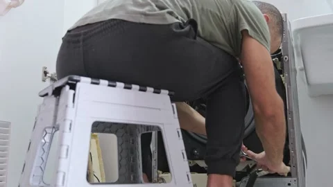 Handyman repairing a broken washing machine with a wrench Stock Footage 328385342