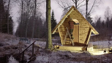 Handyman use ladder to sand window opening of tiny wooden cabin in woods Video stock 296203554