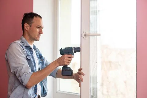 Handyman using a cordless screwdriver to install a window handle. Qualified Stock Photos