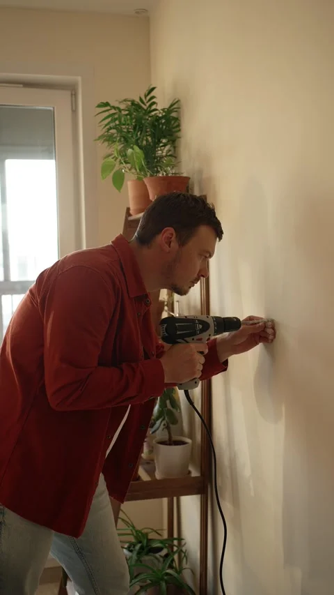 Handyman using an electric drill to make a hole in the wall for mounting a tv Stock Footage 344284635