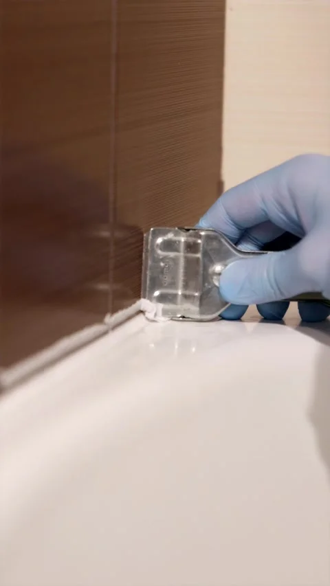 Handyman using sharp razor blade to trim excess silicone sealant from bathr.. Stock Footage 336902499