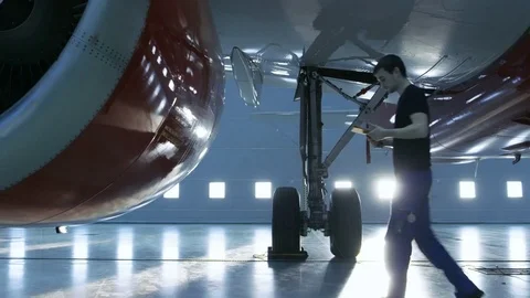 In a Hangar Aircraft Maintenance Young Engineer/ Technician Inspects Plane Stock Footage 77260927