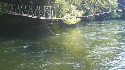 Hanging bridge made with old boards of woods to pass over a small river Stock Footage 135238092