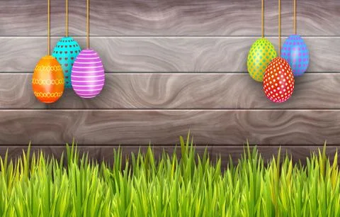 Hanging Easter eggs on rustic background with copy space and border of grass Stock Photos