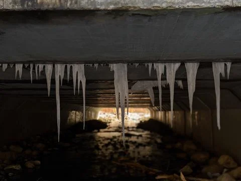 Hanging Icicles Inside a Dark Concrete Tunnel Backlit by Colorful Sunlight 스톡 사진