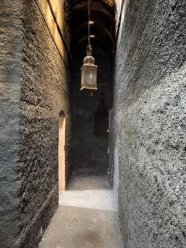 A hanging lantern illuminates a dark stone hallway in a historic building Stockfoto's