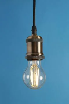 Hanging modern lamp bulb against blue background Stock Photos