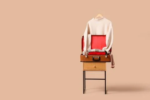 Hanging sweater with suitcase on bedside table against beige background Stock Photos