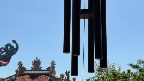 Hanging wind bell moves in the wind near a pagoda roof under open sky. Japanese Stock Footage 336236117