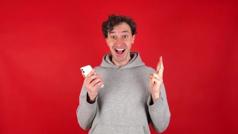 Happily surprised man looking into mobile phone with fingers crossed Видео 304747713