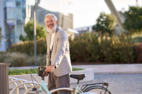 Happy active smiling old senior gray haired man renting bicycle in city park. Stock Photos