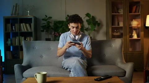 Happy adolescent boy playing a video game on his cellphone at home, mobile app Stock Footage 329838615