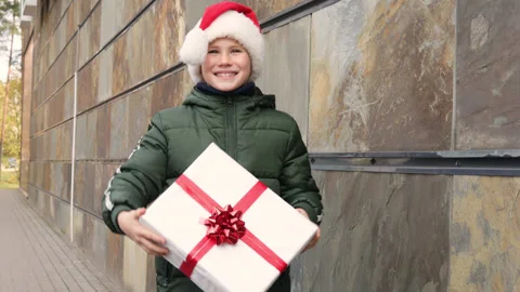 Happy adorable boy in Santa Claus hat showing his Christmas present.Outside Stock Footage 164596853